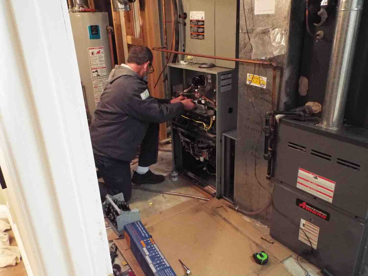 Technician inspecting an HVAC furnace in a utility room, with tools and ductwork nearby