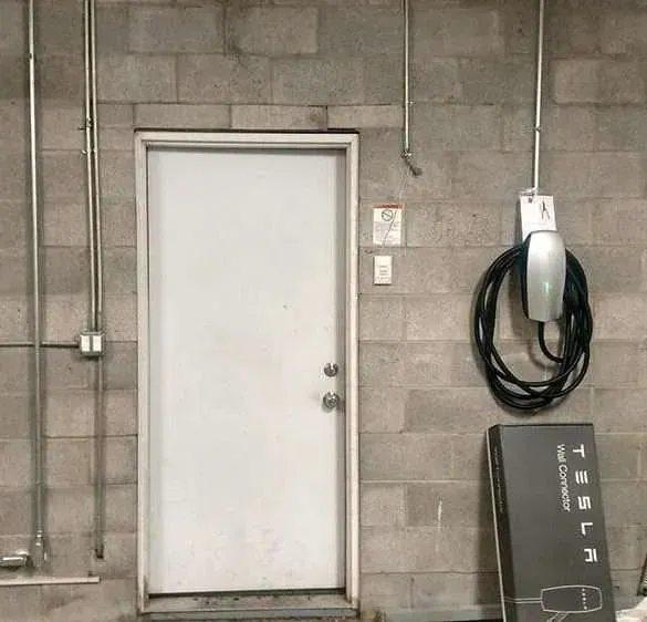 White door in a gray cinderblock wall beside a coiled black EV charging cable.