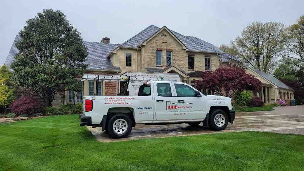 White utility truck parked on a driveway in front of a large stone house with a manicured lawn.