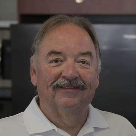 Smiling man with a mustache wearing a white polo shirt indoors