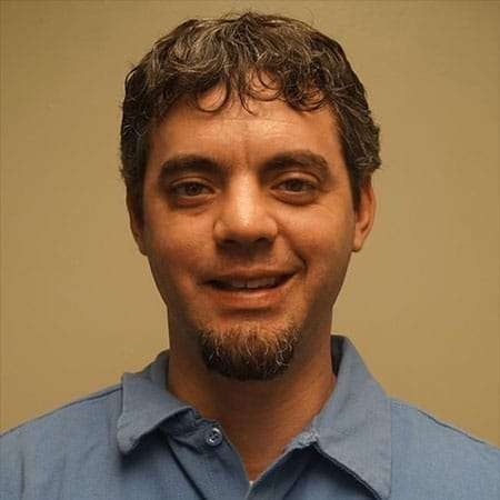 Smiling man in a blue shirt against a plain beige background