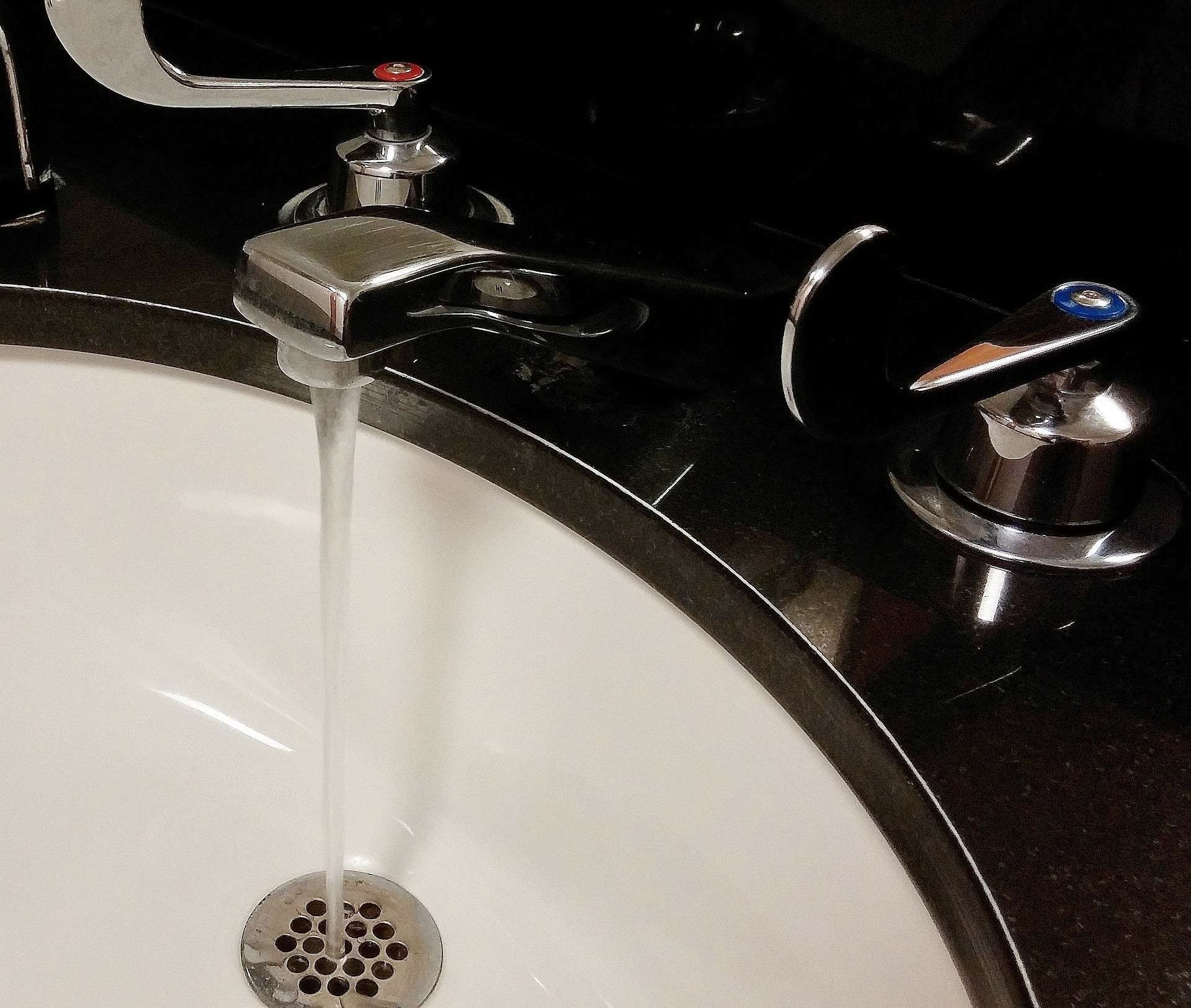 Water running from a chrome faucet into a white sink on a black countertop.