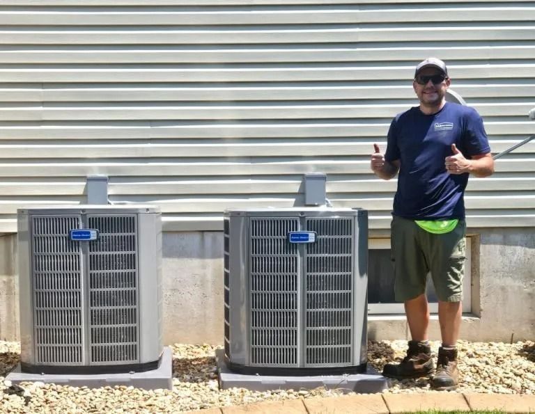 Man standing beside two outdoor air conditioning units against a metal-sided building.