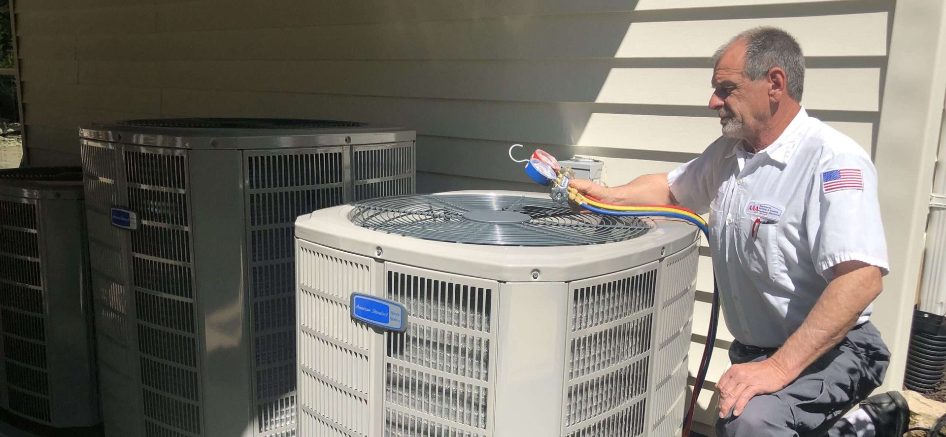 Technician kneels by outdoor HVAC units, inspecting one with a tablet in a sunlit industrial area