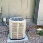 Outdoor air conditioning unit beside a house wall on a concrete pad.