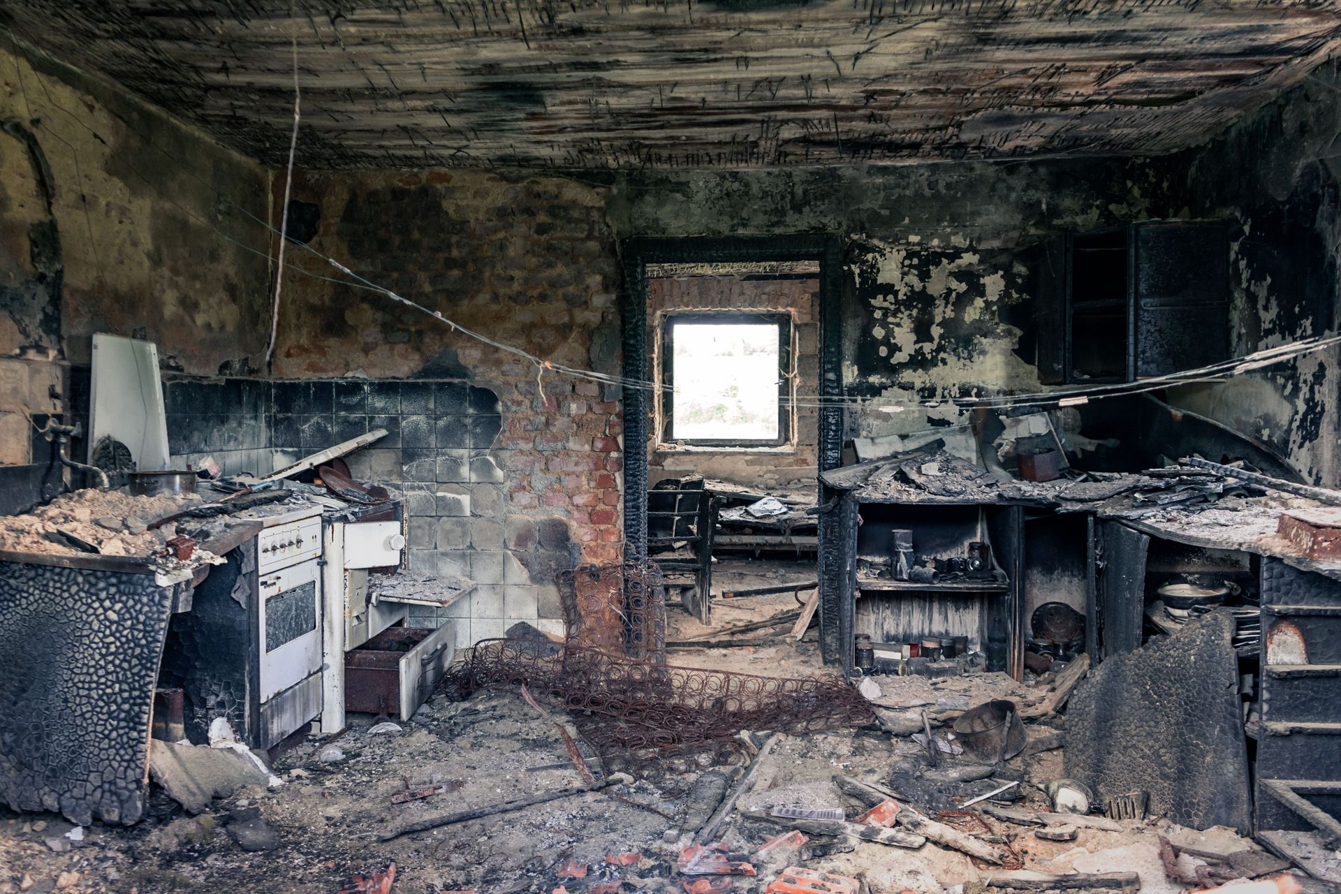 Burned-out room with charred walls, debris, and a window at the back