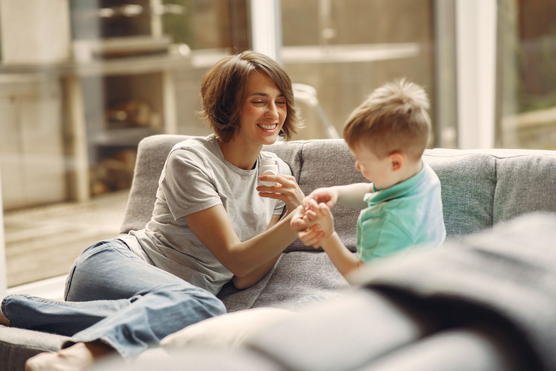 Woman smiling on a couch, playing with a child in a bright living room