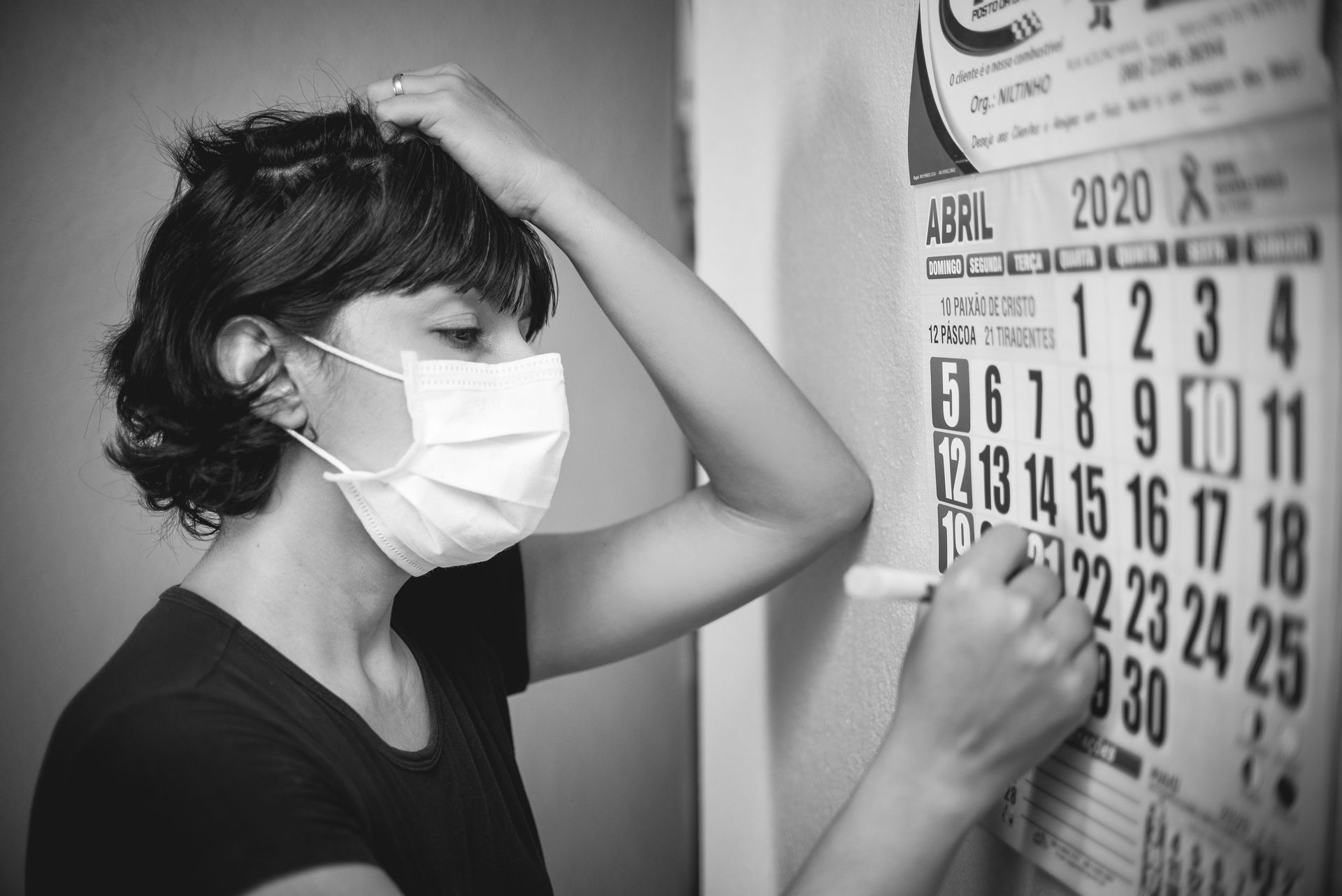 Person wearing a mask writes on a 2020 wall calendar with a marker.