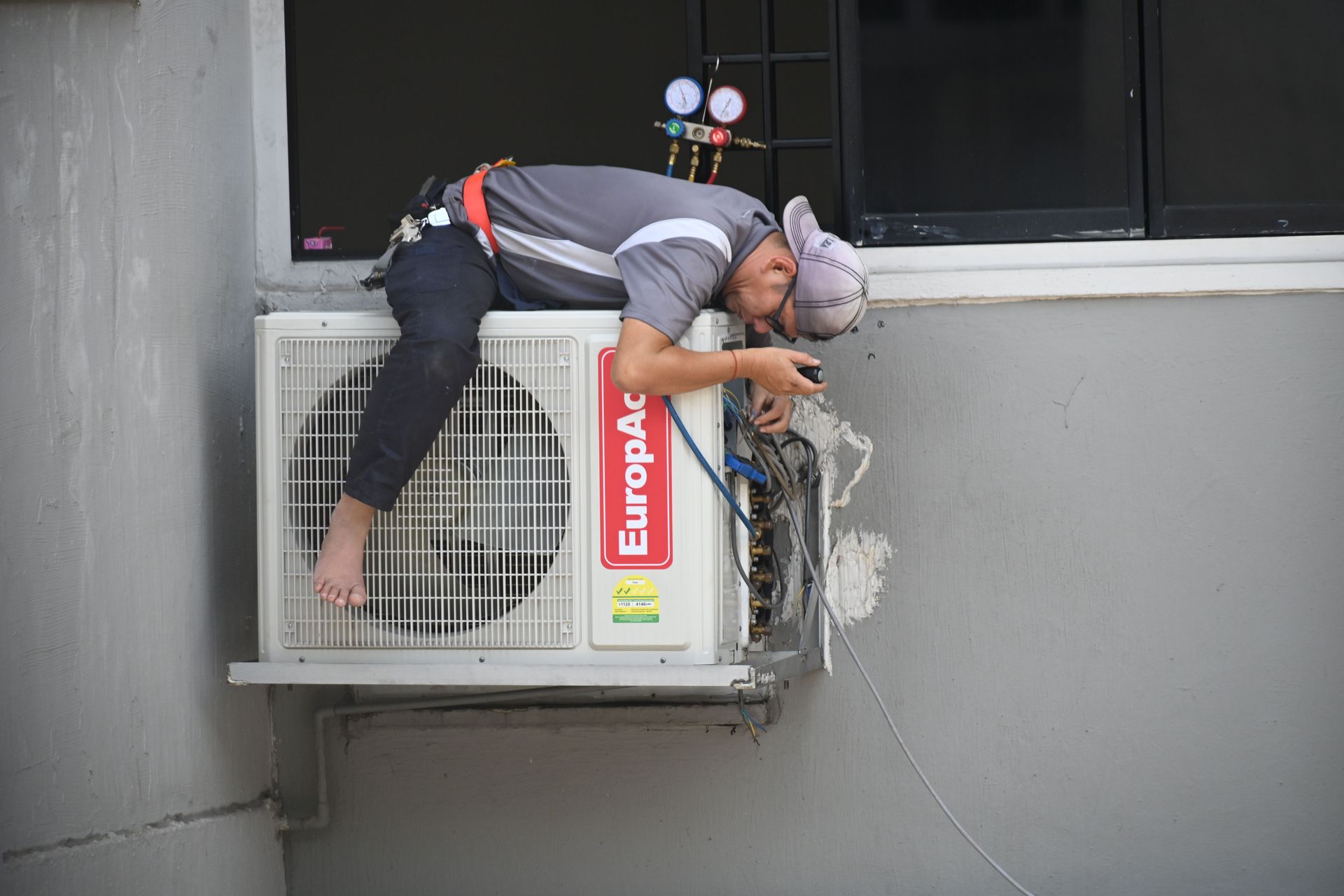 Technician repairing an external air conditioner unit mounted on a gray wall