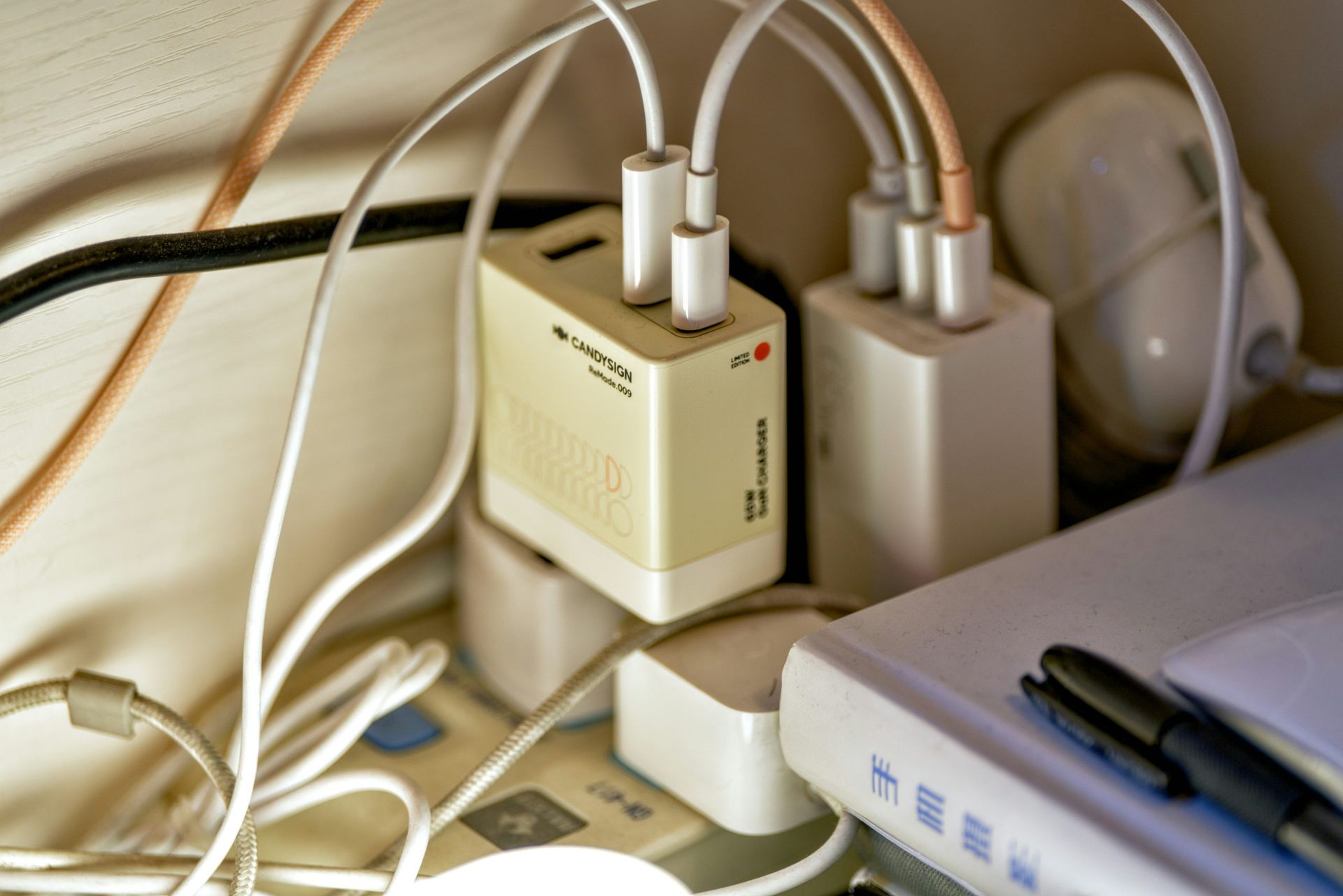 Cords and power adapters tangled on a desk beside a laptop and router near a wall outlet.