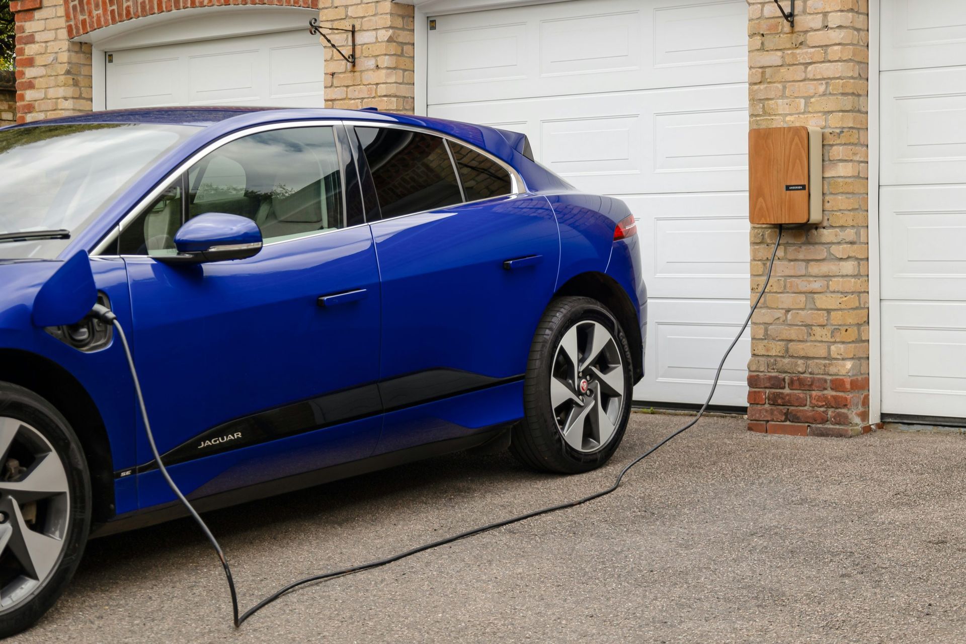 Blue electric SUV charging outside a garage, with cable connected to the front port