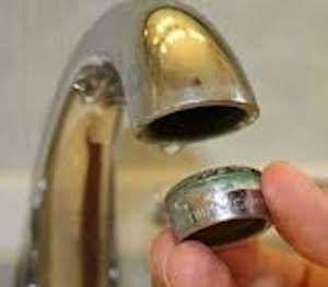 Hand holding a chrome faucet aerator near an open bathroom sink spout