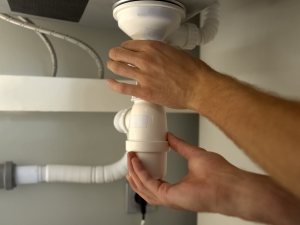 hands opening the p-trap underneath the kitchen sink