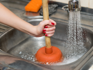 Spotting & Preventing Drainage Clogs 31 orange p[lunger being used to unclog a kitchen sink