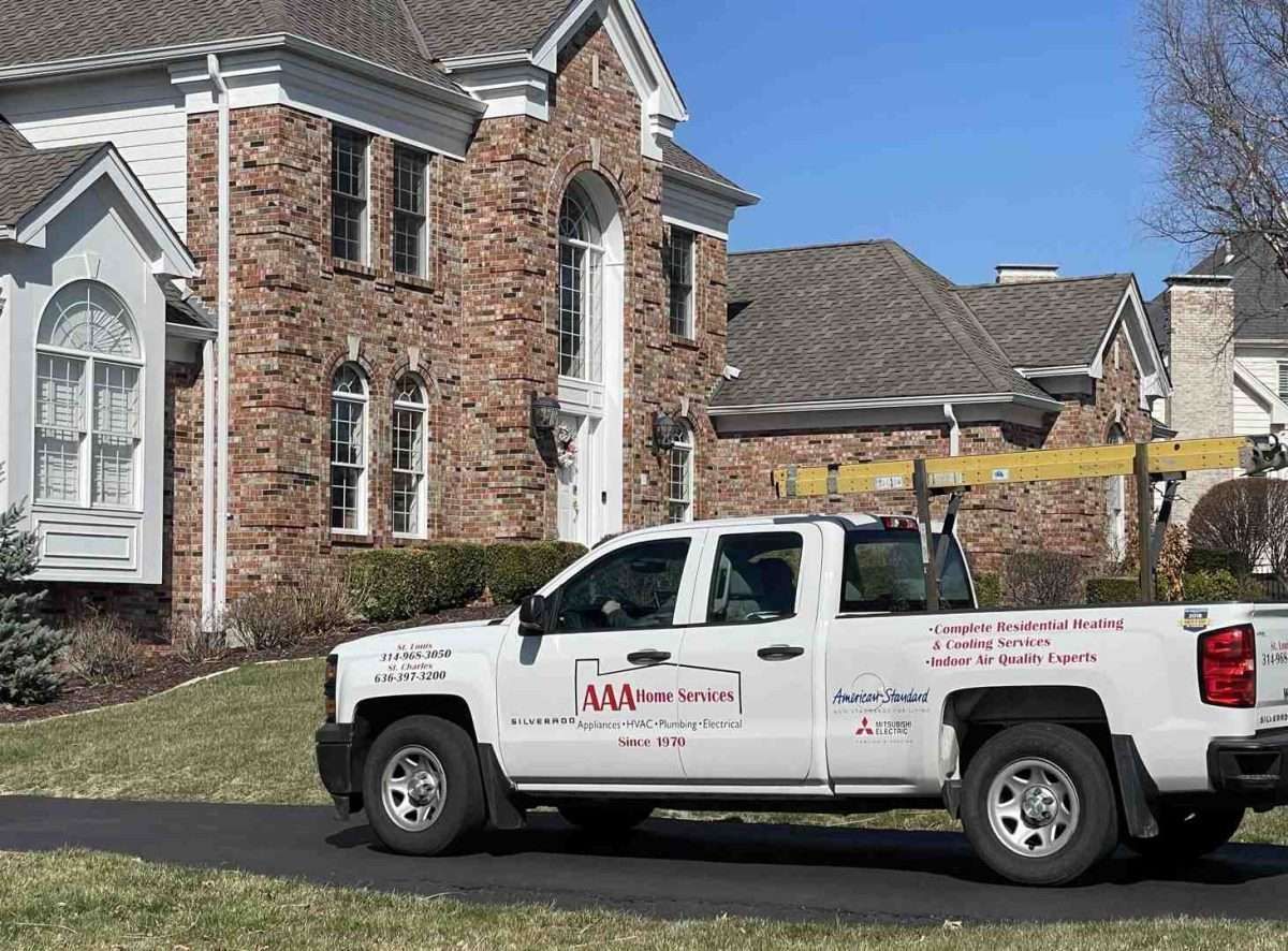 White service pickup truck parked outside a brick residential building under a clear blue sky.