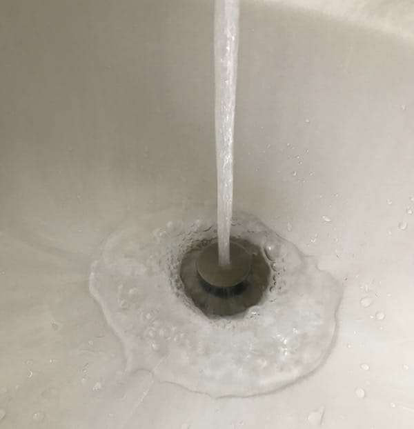 Water flowing into a bathroom sink drain with a small foamy puddle around it
