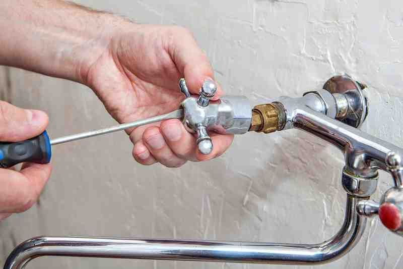 Hands using a wrench to tighten a metal pipe fitting on a wall-mounted faucet.