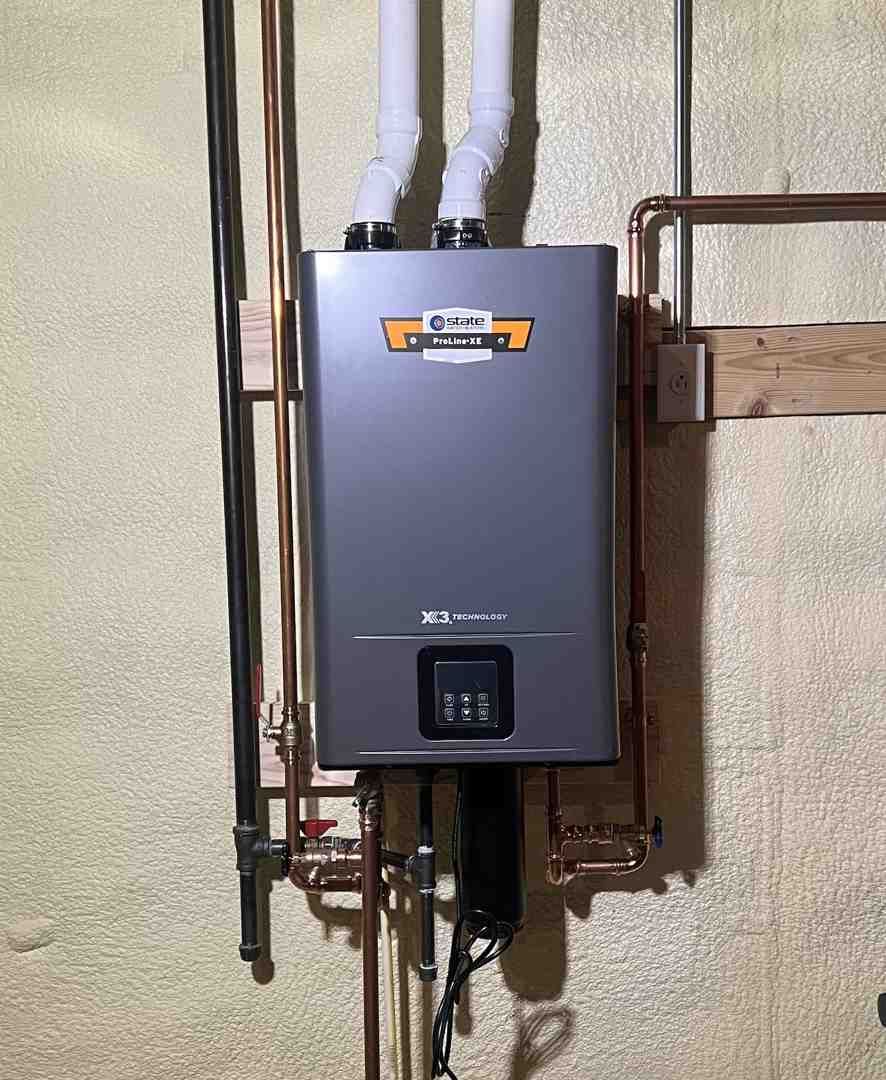 Gray tankless water heater mounted on a wall with copper pipes and vent tubes.