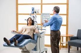 A man is standing next to a woman sitting in a tms therapy chair.