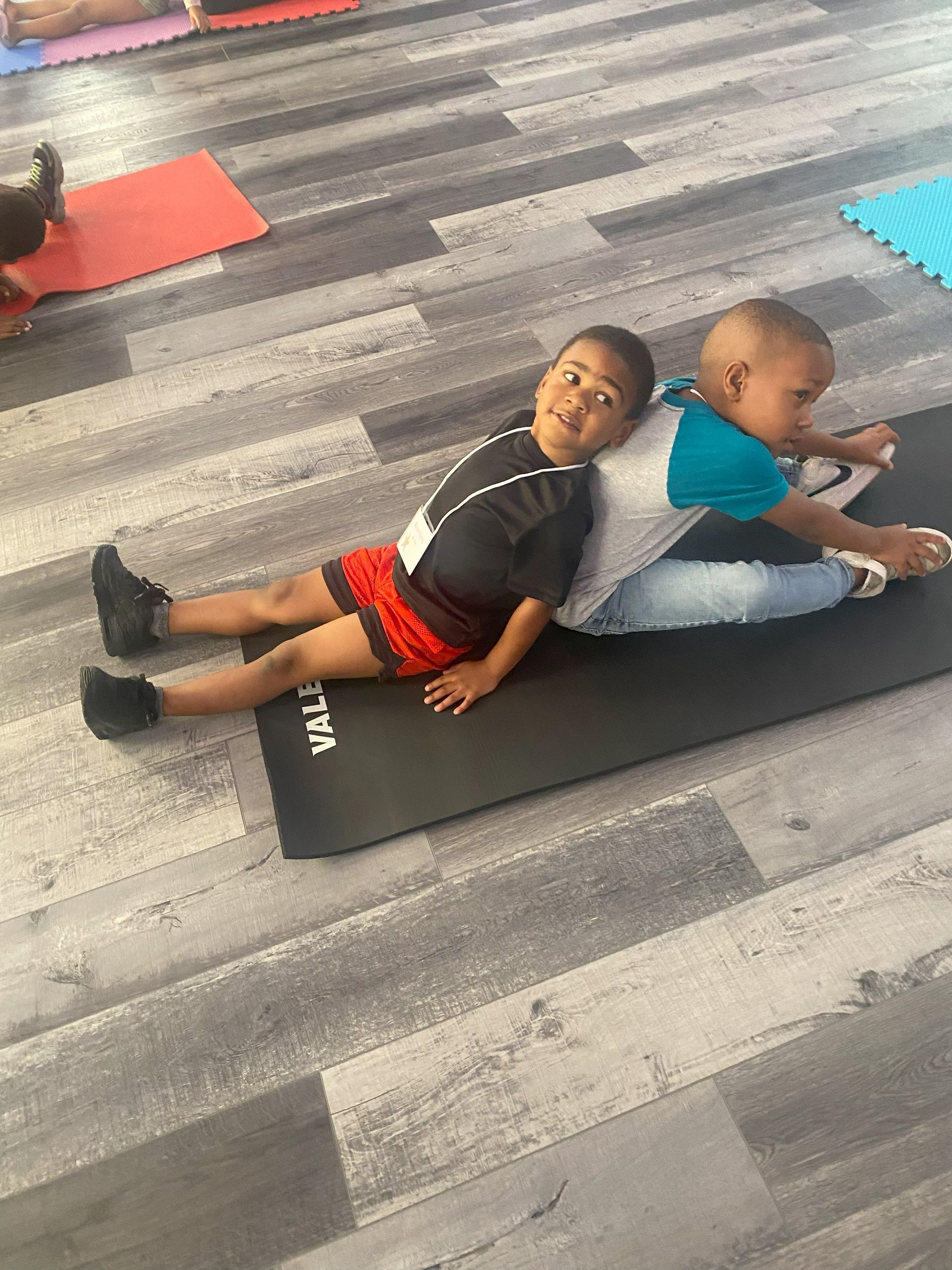 Two young boys are laying back to back on a yoga mat.