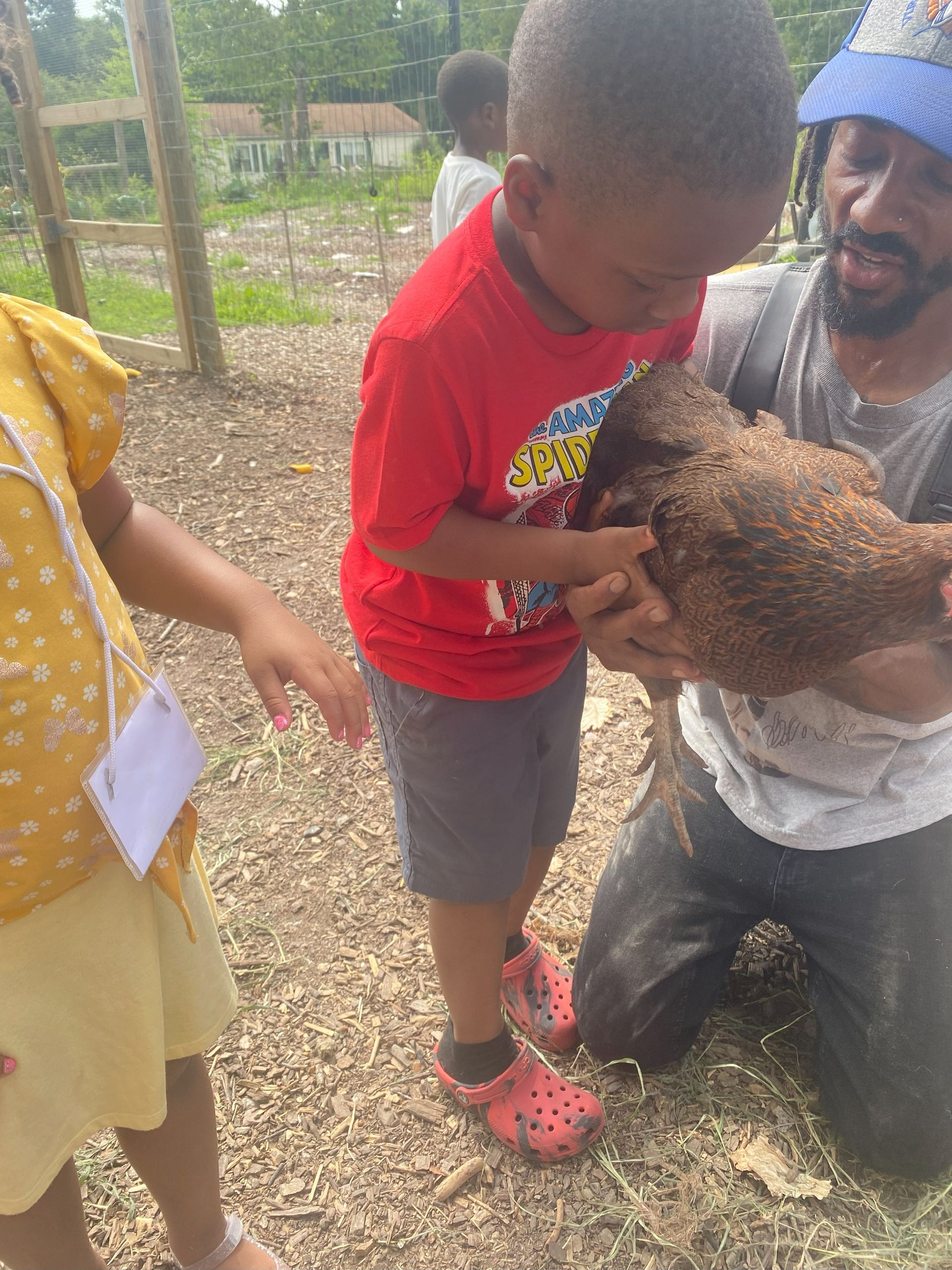 A man is kneeling down holding a chicken while a little boy looks on.