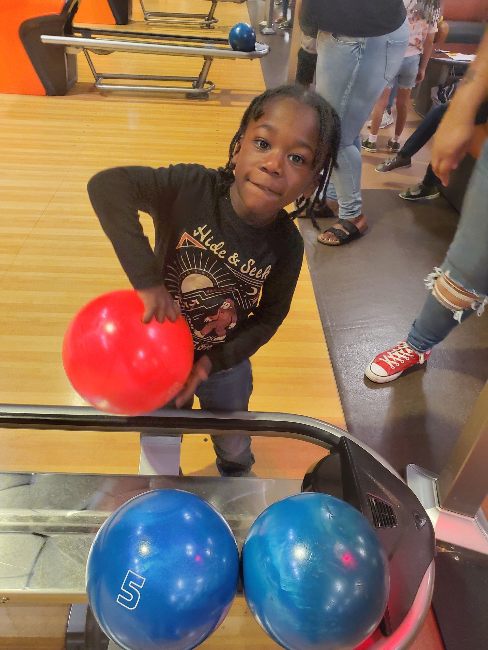 A little girl is holding a red bowling ball in a bowling alley