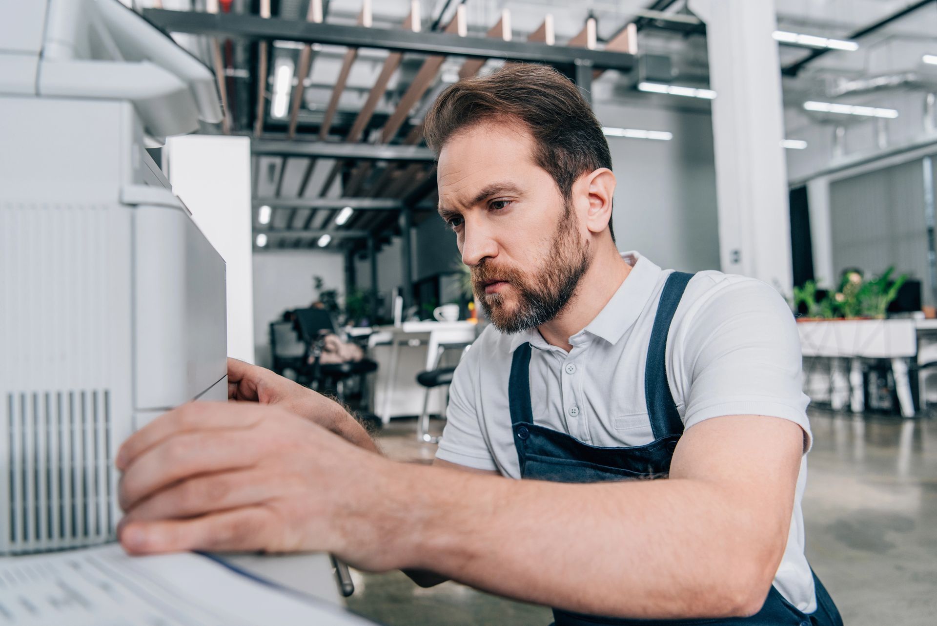 Uomo in abiti da lavoro che ripara una grande stampante da ufficio.