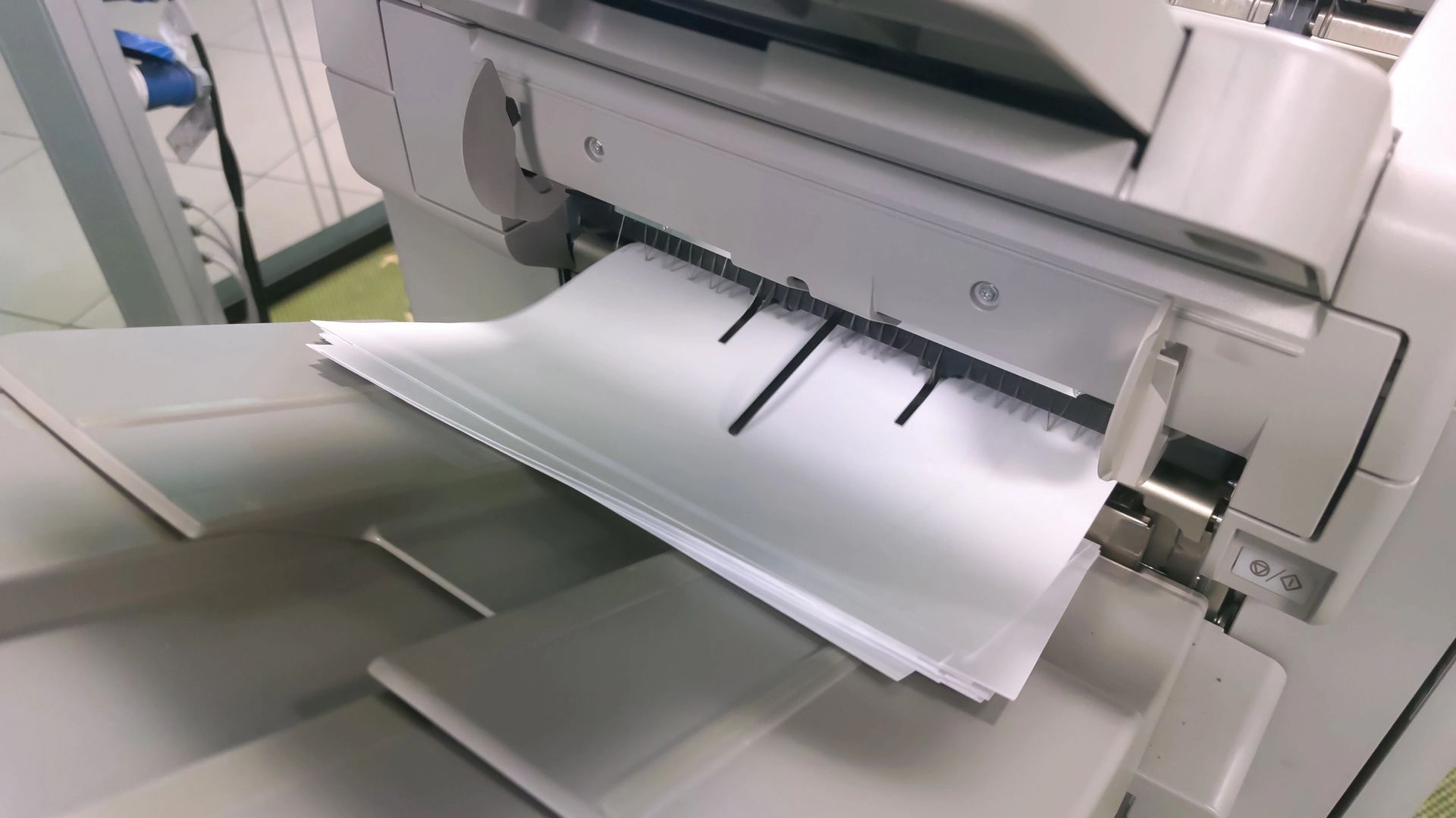 Fogli di carta bianca inseriti in una macchina bianca e grigia, probabilmente una fascicolatrice o una fotocopiatrice.