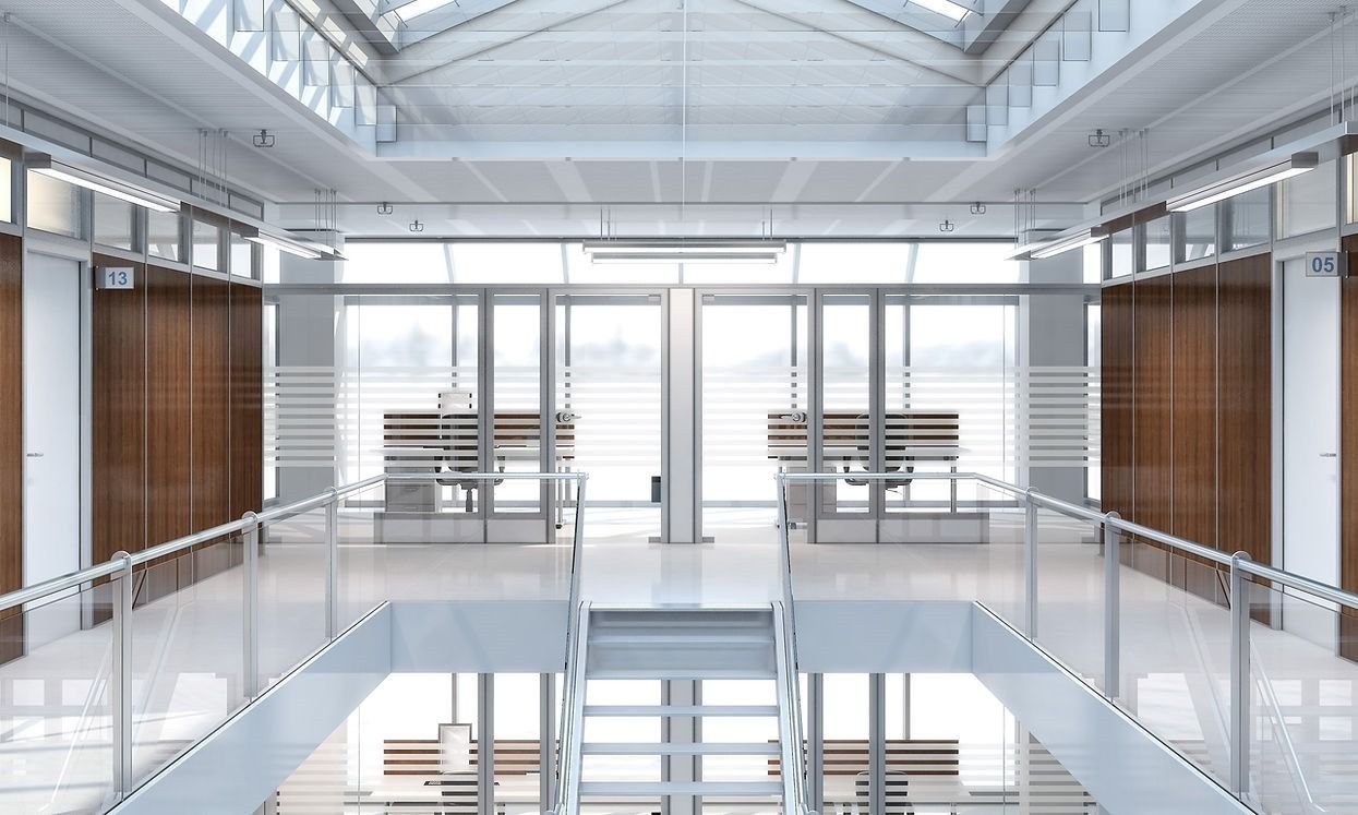 Un interno per ufficio luminoso e moderno con una scala centrale, ringhiere in vetro e postazioni di lavoro individuali addossate a pareti in legno.