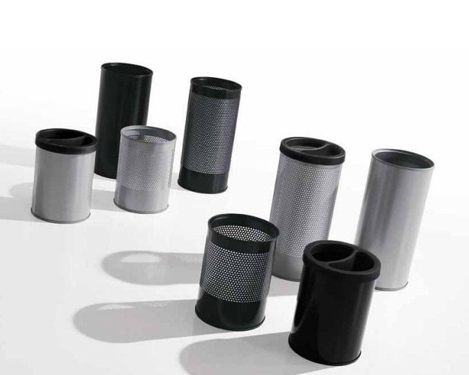 Un gruppo di organizer da scrivania cilindrici, assortiti in nero e argento e con diverse texture, disposti su una superficie bianca.