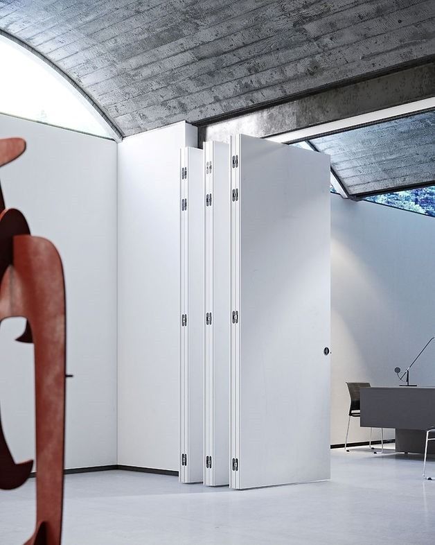 Una moderna porta divisoria pieghevole bianca in un ufficio minimalista con soffitto a volta in cemento texturizzato.