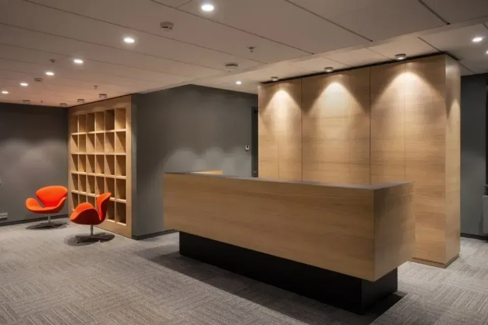 Una moderna area reception per ufficio con una scrivania in legno chiaro, una scaffalatura abbinata e due poltrone lounge di colore arancione acceso.