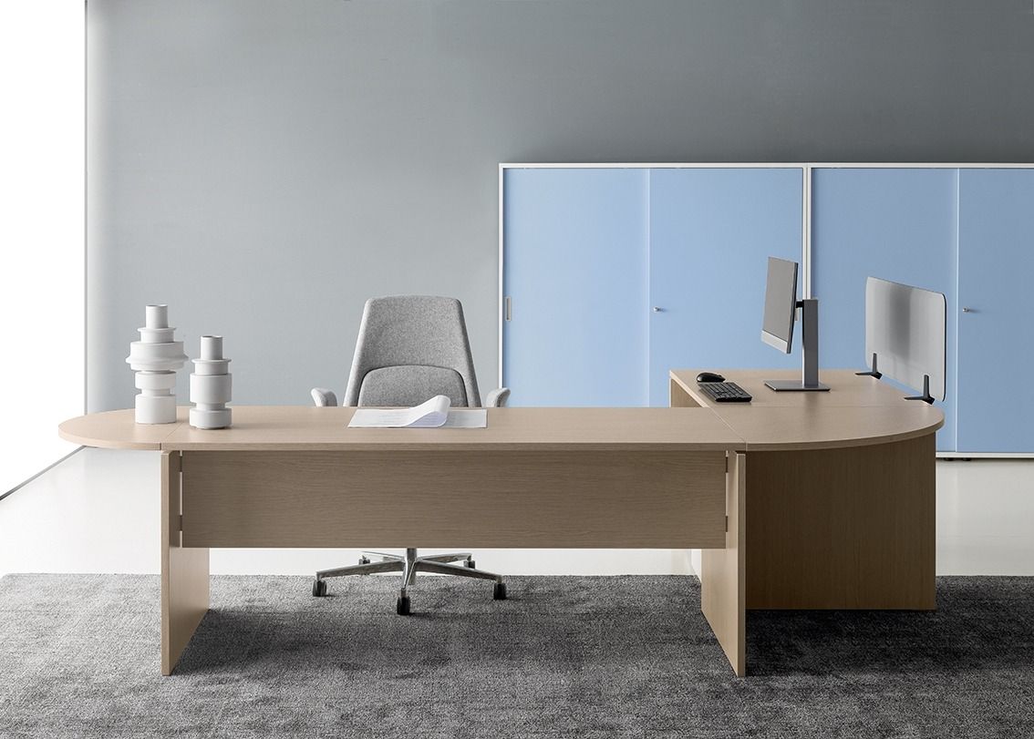 Una scrivania a L in legno chiaro con sedia abbinata è posizionata su un tappeto grigio davanti a un mobile contenitore blu.