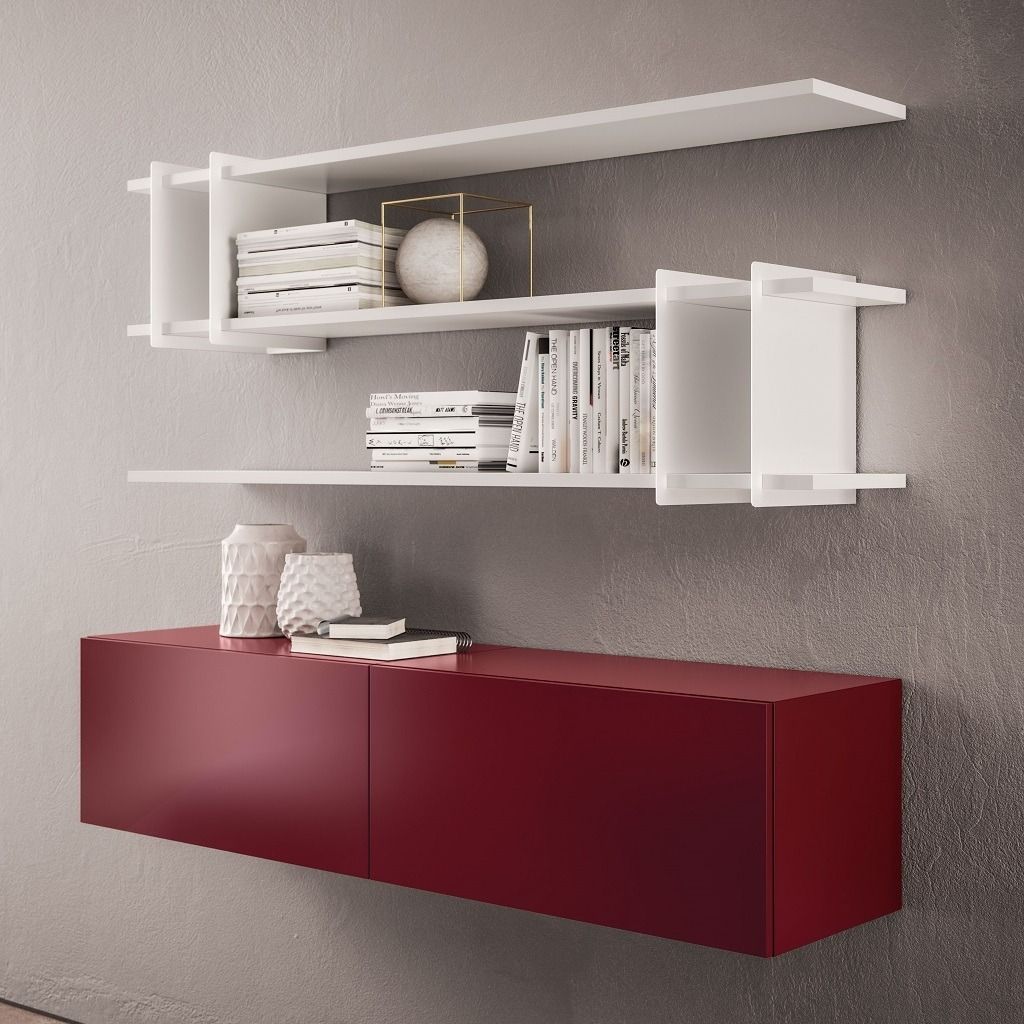 Sotto una parete grigia, sotto delle mensole bianche a parete che ospitano libri e oggetti decorativi, si trova un mobiletto rosso a muro.