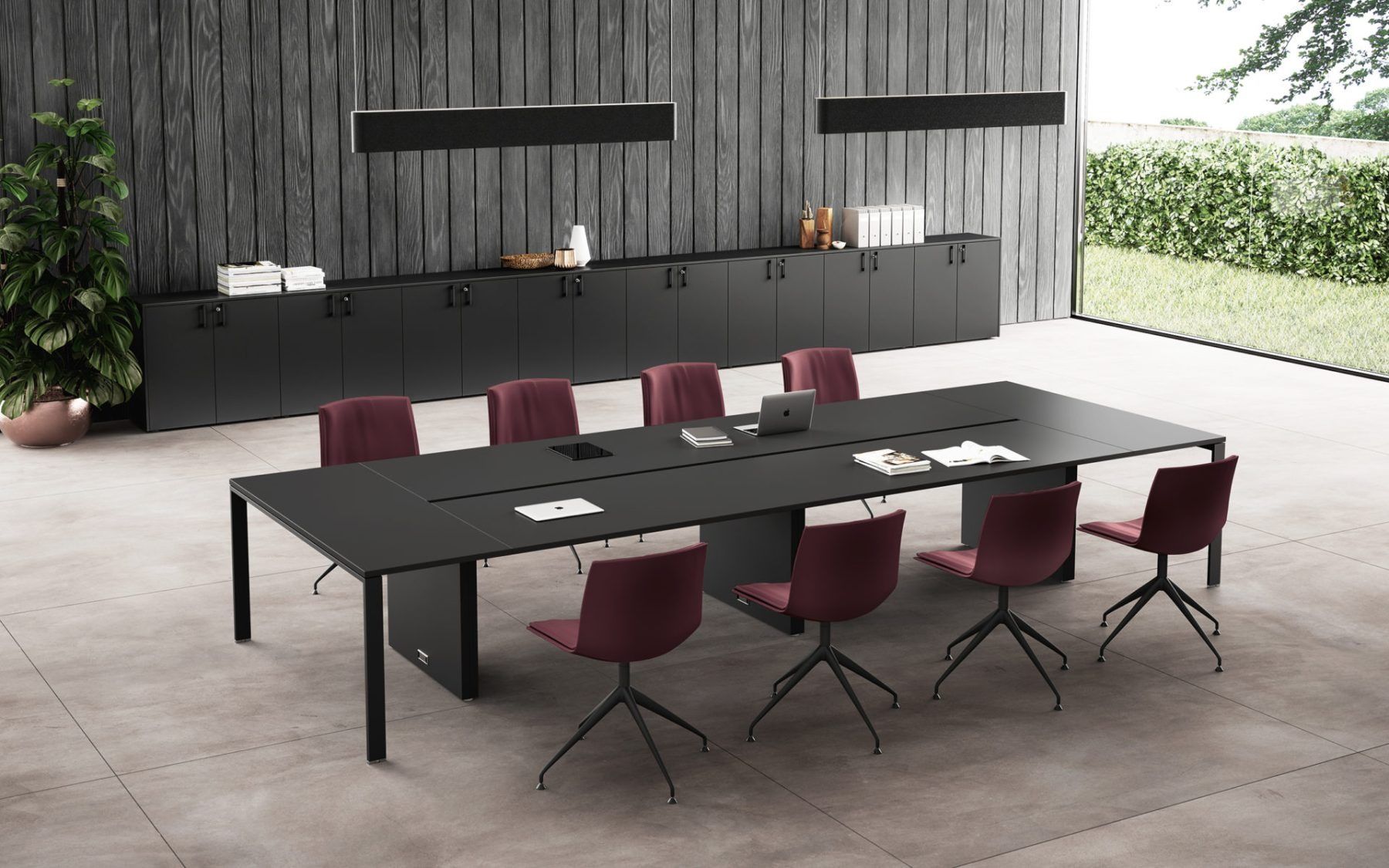 Un lungo tavolo da conferenza nero con dieci sedie rosso scuro in un ufficio moderno con pareti in legno scuro e pavimento in cemento.