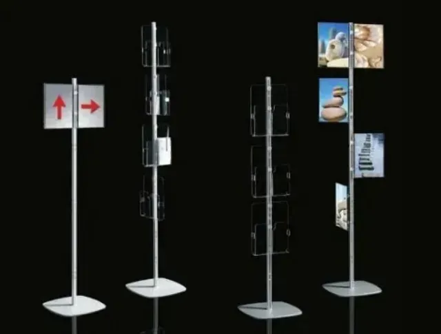 Quattro supporti da pavimento in metallo su sfondo nero, che espongono cartelli, portadepliant e opere d'arte incorniciate.