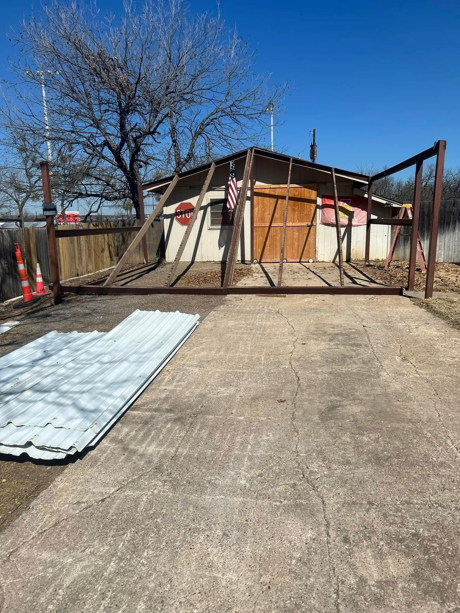 A metal frame construction structure stands in front of a small building with a wooden door, under a clear blue sky.