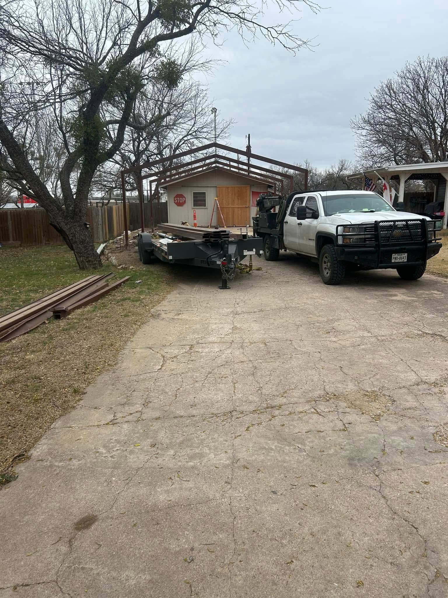 A white pickup truck with a large black grill guard is parked in a gravel driveway next to a small utility trailer.