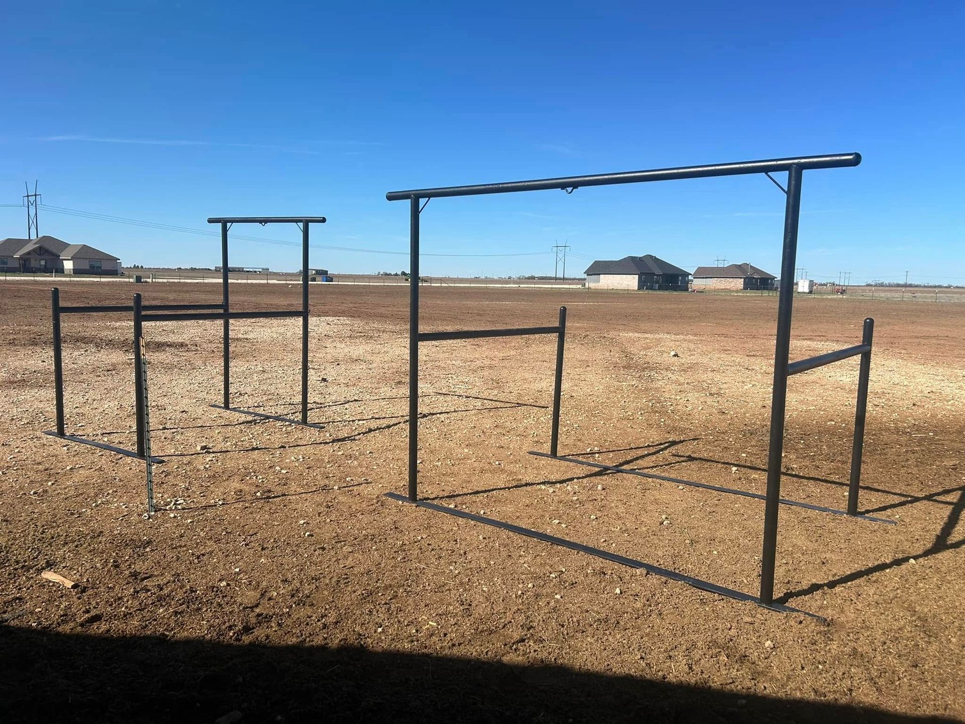 Two black metal outdoor fitness structures stand on a dry, rocky field under a clear blue sky.