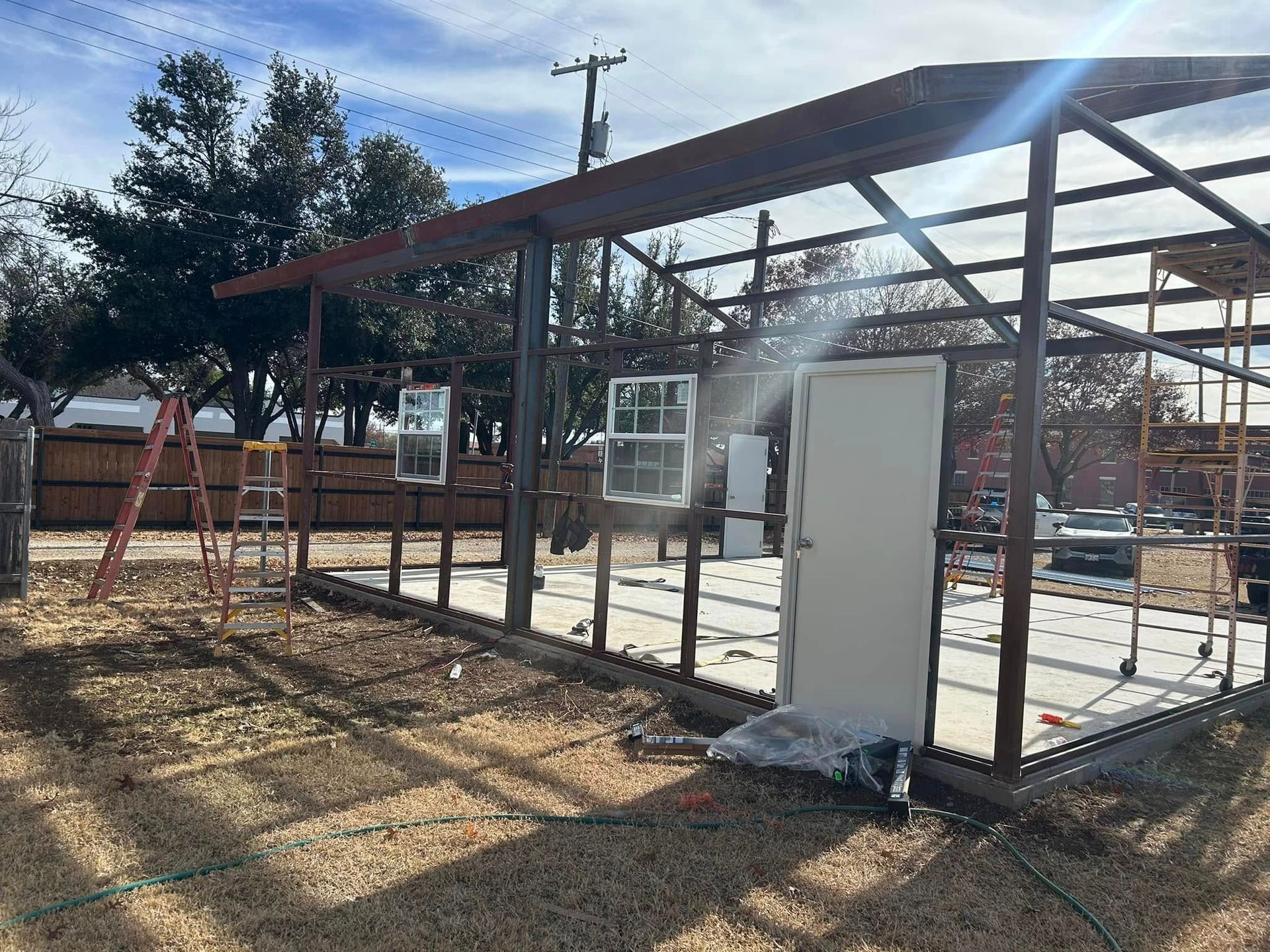 Construction site featuring a metal building frame, a white door, and installed window frames on a concrete slab.