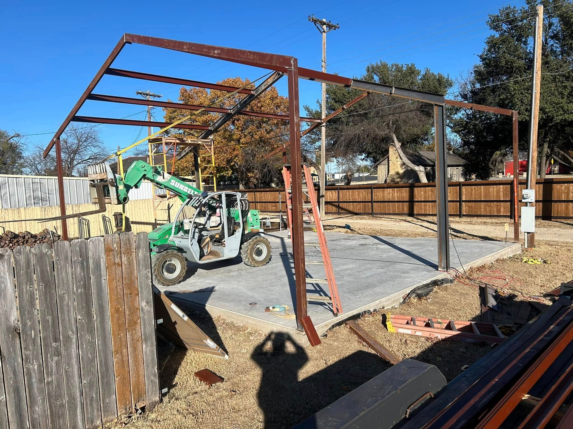 A green telehandler parked inside the steel frame of a building under construction on a sunny day.