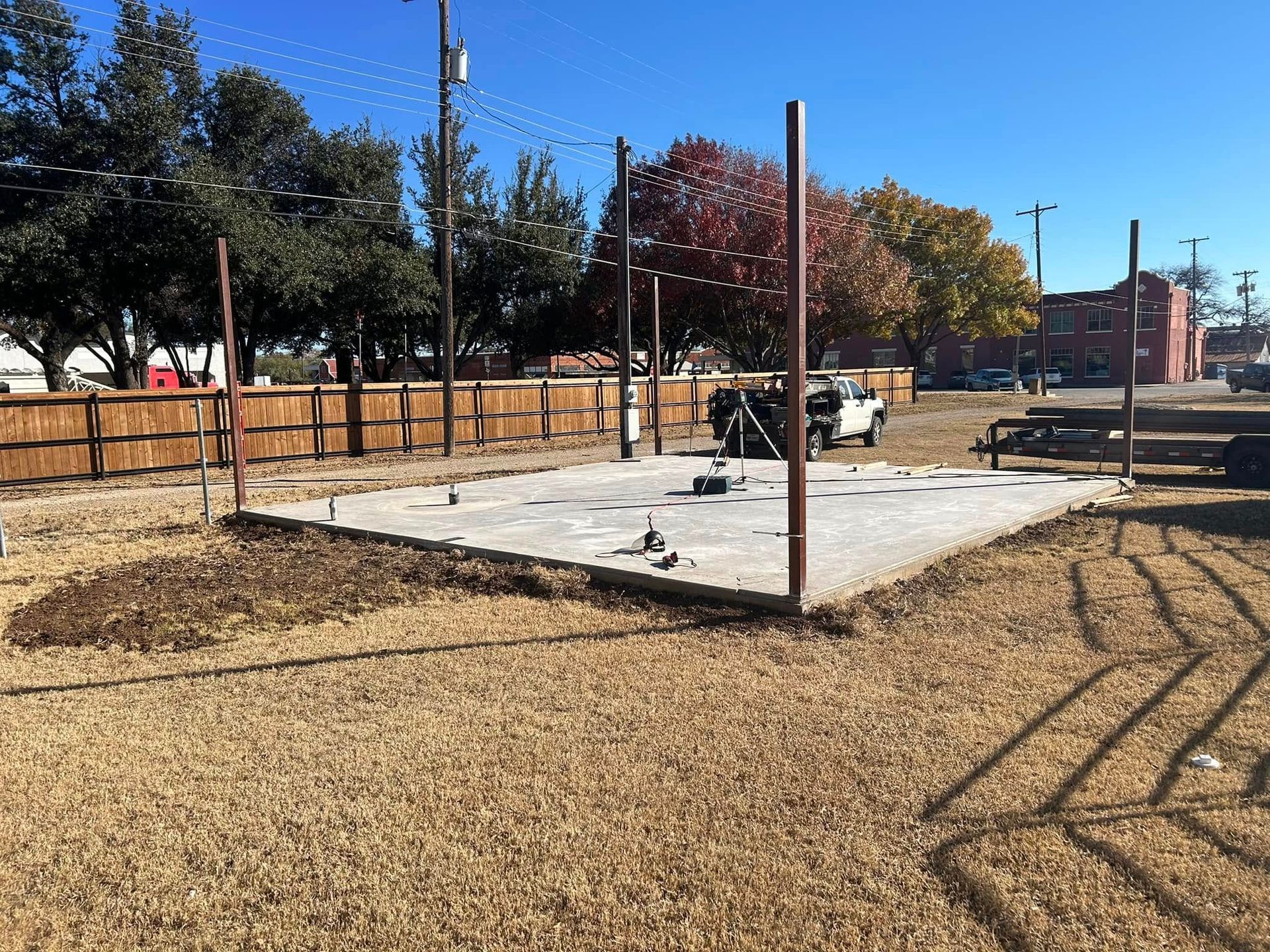 A rectangular concrete foundation slab with several upright metal support poles stands in a dry, grassy field.