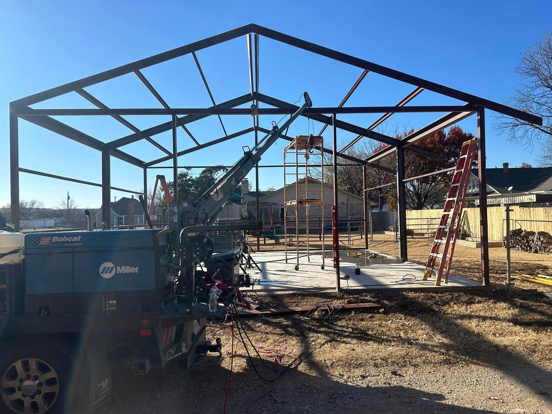 Steel frame of a building under construction on a sunny day, with a welder vehicle and red ladder on site.