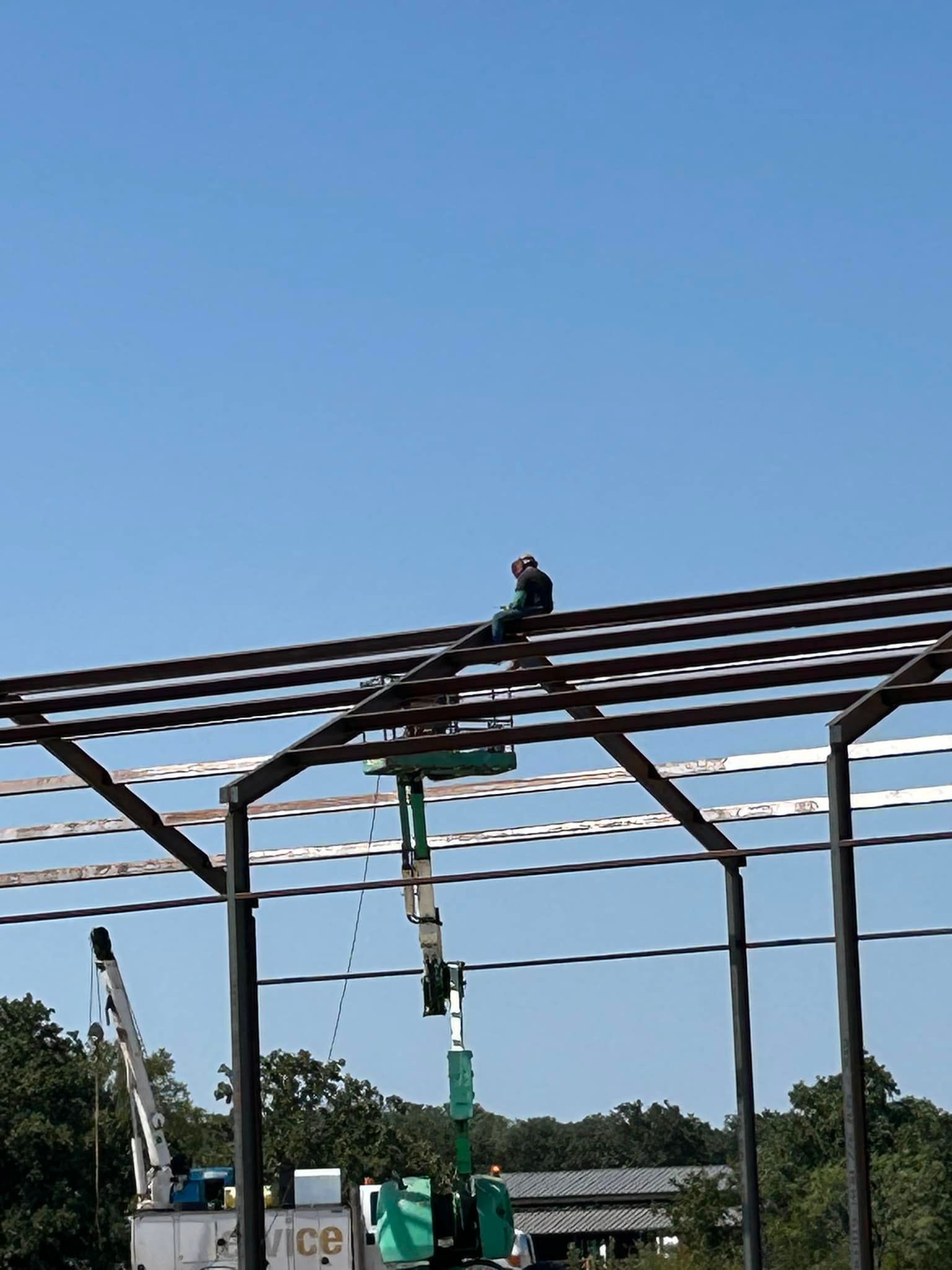 A construction worker in a green boom lift works on the steel frame of a building under a clear blue sky.