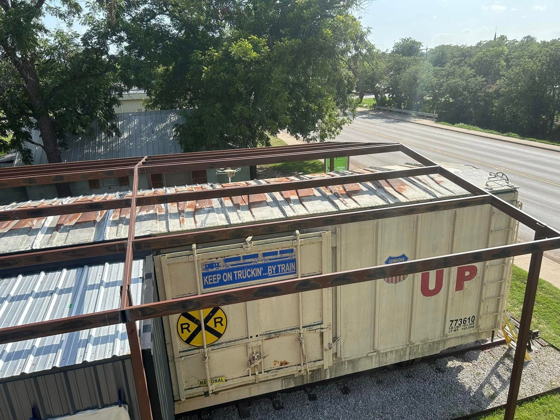 An elevated view of a repurposed Union Pacific train car standing next to a metal building near a road and trees.