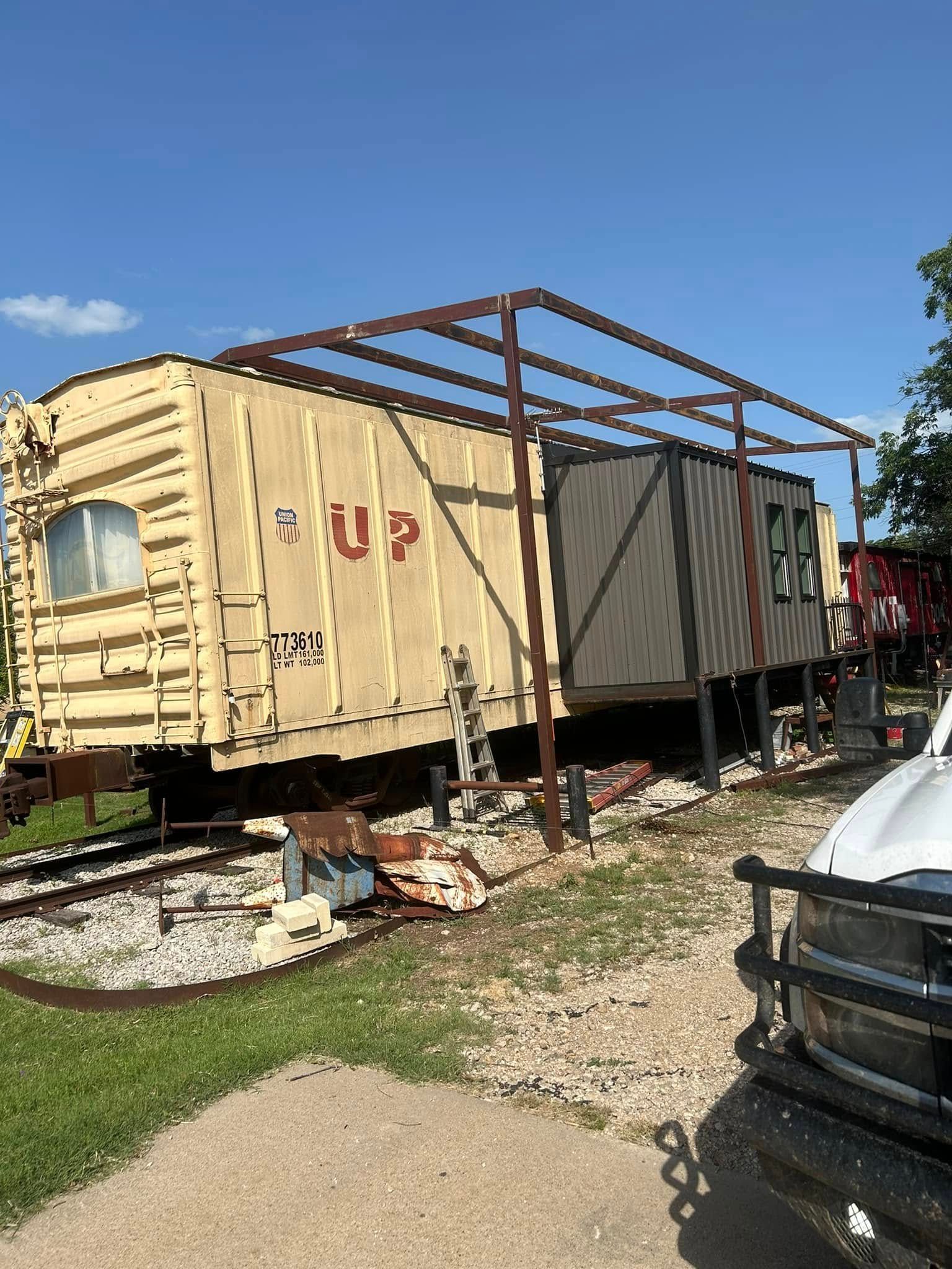 A yellow Union Pacific rail car sits on tracks under a metal framework with a white vehicle in the foreground.