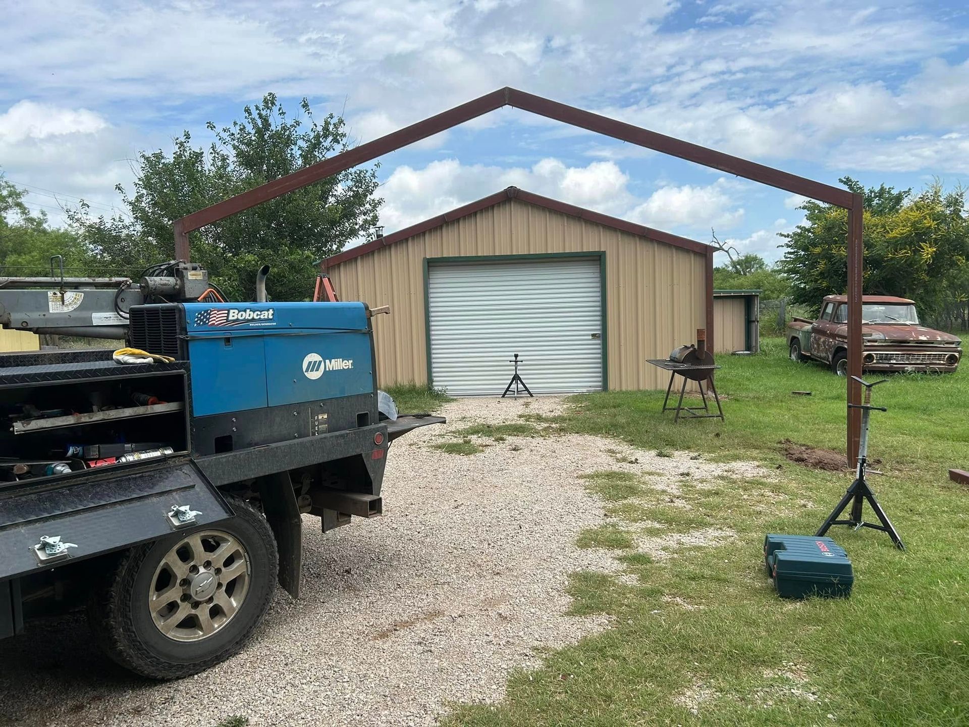 A welding rig parked in front of a metal building, with a steel frame arch set up in the yard.