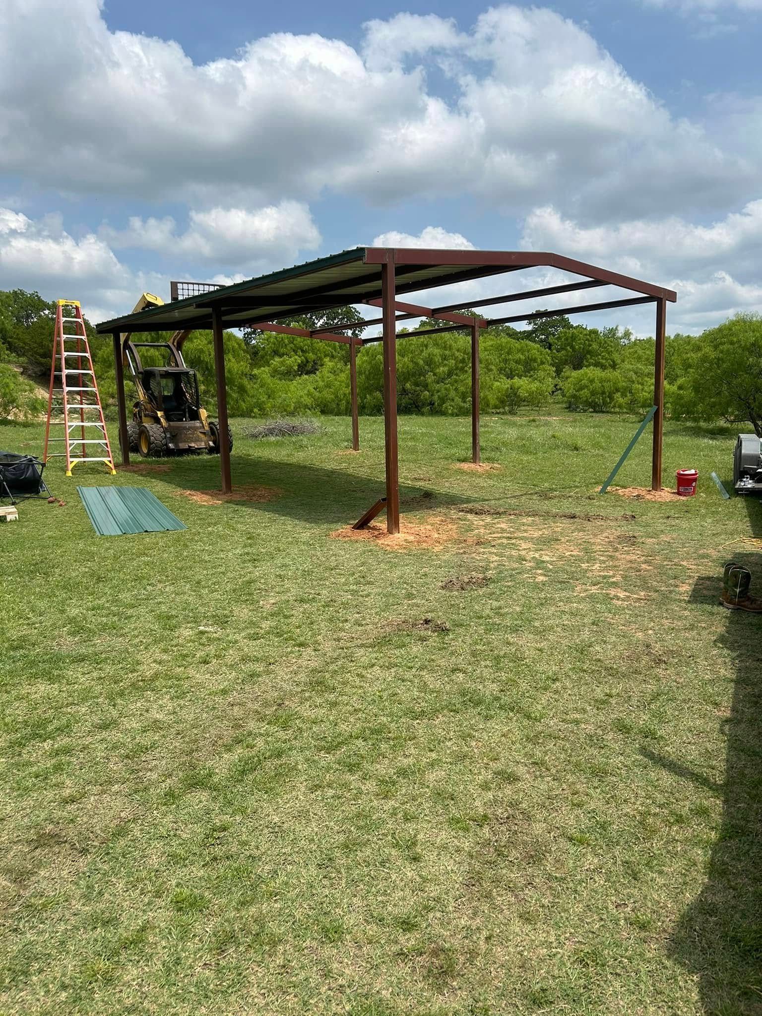 A metal frame structure for a carport under construction in a grassy field with a ladder and equipment nearby.