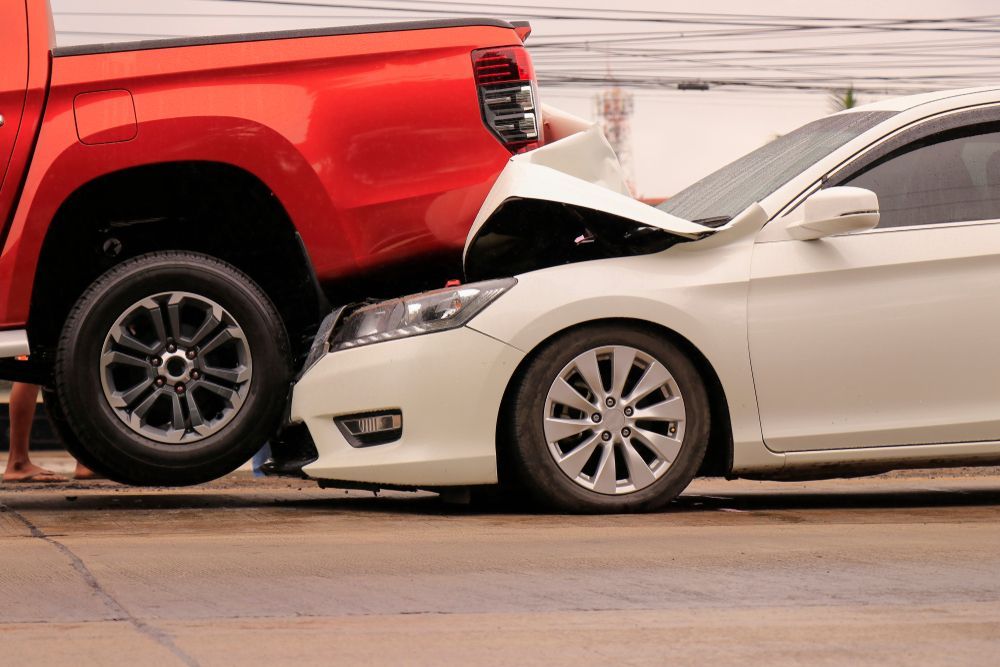 Red pickup truck rear-ended a white sedan on a street, showing front-end damage.