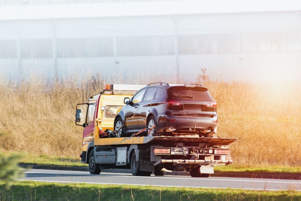 Tow truck hauling a black SUV on a flatbed along a roadside